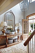 Hallway in French country-house style with ornately framed mirror above console table and pair of lamps