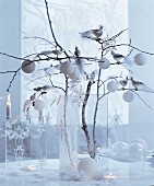 weiße Weihnachten: Zweige in Glasvase dekoriert mit Baumkugeln, Sternanhängern und silbernen Dekovögeln