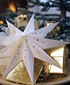 Decorative paper star with perforated pattern and gifts wrapped in gold paper on wooden plate