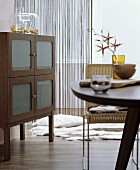 Dining table, wicker chair and sideboard with frosted glass door panels in interior in shades of brown