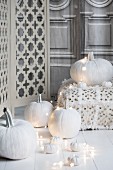 Halloween arrangement of white-painted pumpkins, fairy lights and floor cushions