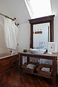 Dark wooden washstand below mirror and skylight next to wood-clad bathtub with shower curtain