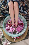 Woman bathing feet in bowl of water and flowers