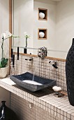 Lion's-head water-spout tap above tiled washstand with dark grey stone basin