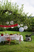 Set table under white lanterns hung from tree for Swedish crayfish-season garden party