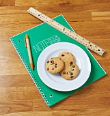 Chocolate chip cookies on a notebook with a ruler and a pencil