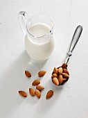 Almond milk in a glass jug next to a spoon of almonds