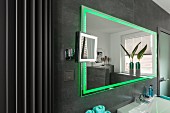A wall mirror with integrated green LED lighting on a grey-tiled wall