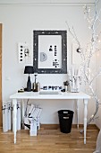 Fairy lights on white-painted branch next to white desk with black accessories