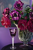 Purple, crystal liqueur glass next to vase of flowers in various shades of red
