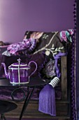 Purple teapot on side table in front of antique bench with purple tassel and scatter cushion