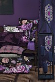 Stack of cushions with different covers on floor and on antique bench against purple wall