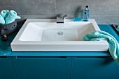 A white sink built with a modern tap in to a petrol-coloured washstand