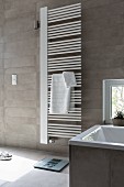 A white hand towel heater on a grey-tiled wall in a modern bathroom
