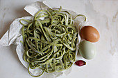 Fresh spinach linguine, eggs and a garlic clove on a marble surface