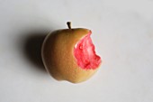 A pink pearl apple with a bite taken out of it on a marble surface