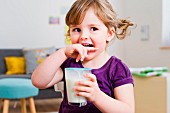 A little girl with pigtails holding a glass of milk