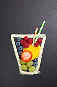 A chalk drawing of a glass filled with real fresh fruit and straws
