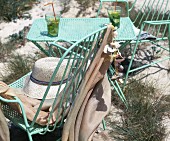 Erfrischungsgetränke am Strand, Tisch aus türkis lackiertem Metall und passende Stühle, darauf Sonnenhut