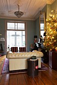 Beleuchteter Weihnachtsbaum im Wohnzimmer mit Stuckdecke und Chesterfieldsofa