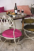 Metal bistro chairs with round seat cushions at antique wooden table set with bread and wine