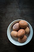 Angestossene Eier für Soleier in Keramikschale auf Holztischplatte
