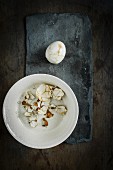 A peeled pickled egg with a linen patter on a slate surface with egg shell in a ceramic bowl on a wooden surface