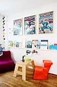 Children's books on wall-mounted shelves, framed comic posters and bold orange child's chair in Scandinavian interior