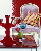 Pastel, Baroque armchair with yellow-striped cushion against red background and brightly coloured glasses on red table