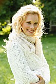 A young woman wearing a white, coarse-knit cardigan and scarf