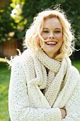 A young woman wearing a white, coarse-knit cardigan and scarf