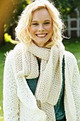 A young woman wearing a white, coarse-knit cardigan and scarf
