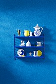 Crockery on a blue shelf on a wall with a blue faux uni patterned wallpaper