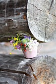 Posy of wild flowers in cup on log