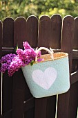 Lilac flowers in shopping basket hanging on wooden garden fence