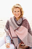 A blonde woman wearing a woollen shawl on a beach