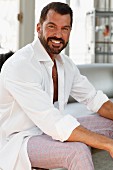 A dark-haired man with a bread wearing a white shirt and checked trousers