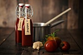 Bottle of homemade ketchup with ingredients and kitchen utensils on a wooden table