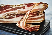 A piece of bacon on a board with a slice cut off