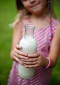 A little girl in a garden holding a bottle of vegan milk