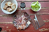 A rustic meat platter with bread, red wine and lettuce