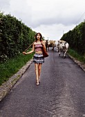 A woman wearing a strapless top and a mini skirt walking in front of a herd of cows