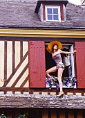 Young woman wearing shorts and a bandeau top climbing out of a window