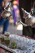 Peppermint tea being poured from silver teapots into tea glasses