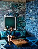 Pattern mix in shades of blue: Young woman on a sofa in the living room with differently wallpapered walls