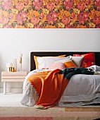 Doppelbett mit orangefarbenen Farbakzenten, Blumentapete über weißem Sockel