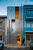 Narrow, three-storey town house with flexible façade made from stainless-steel shutters and illuminated interior at twilight