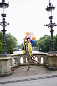 Frau mit Kleidung im Retrostil mit Luftballons auf Brücke