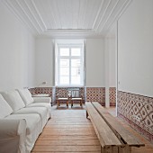 White sofa against wall opposite rustic wooden bench in white living room with tiled dado