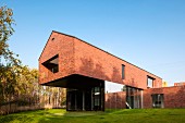 Zeitgenössisches Wohnhaus mit auskragendem Obergeschoss in Ziegelbauweise, in sonnenbeschienenem Garten